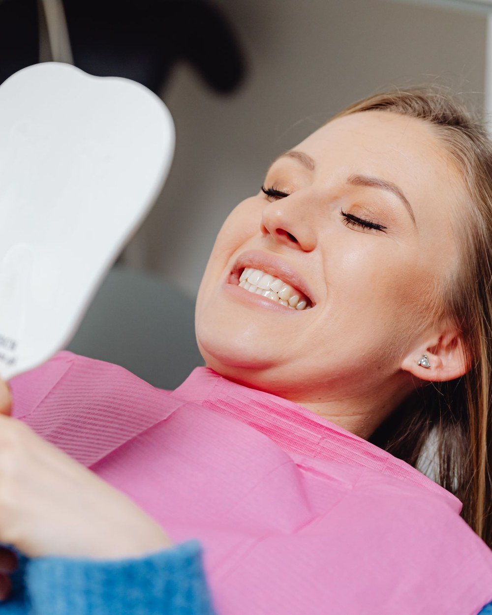 Patient viewing her new smile in a hand mirror after cosmetic dental treatment at The Port Dental Clinic Calgary NE