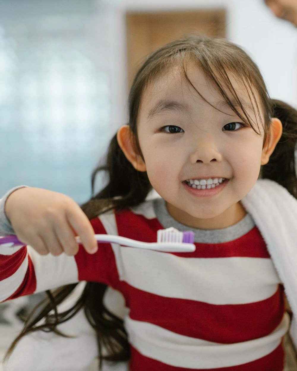 Young child with healthy teeth holding a toothbrush, building good oral habits early