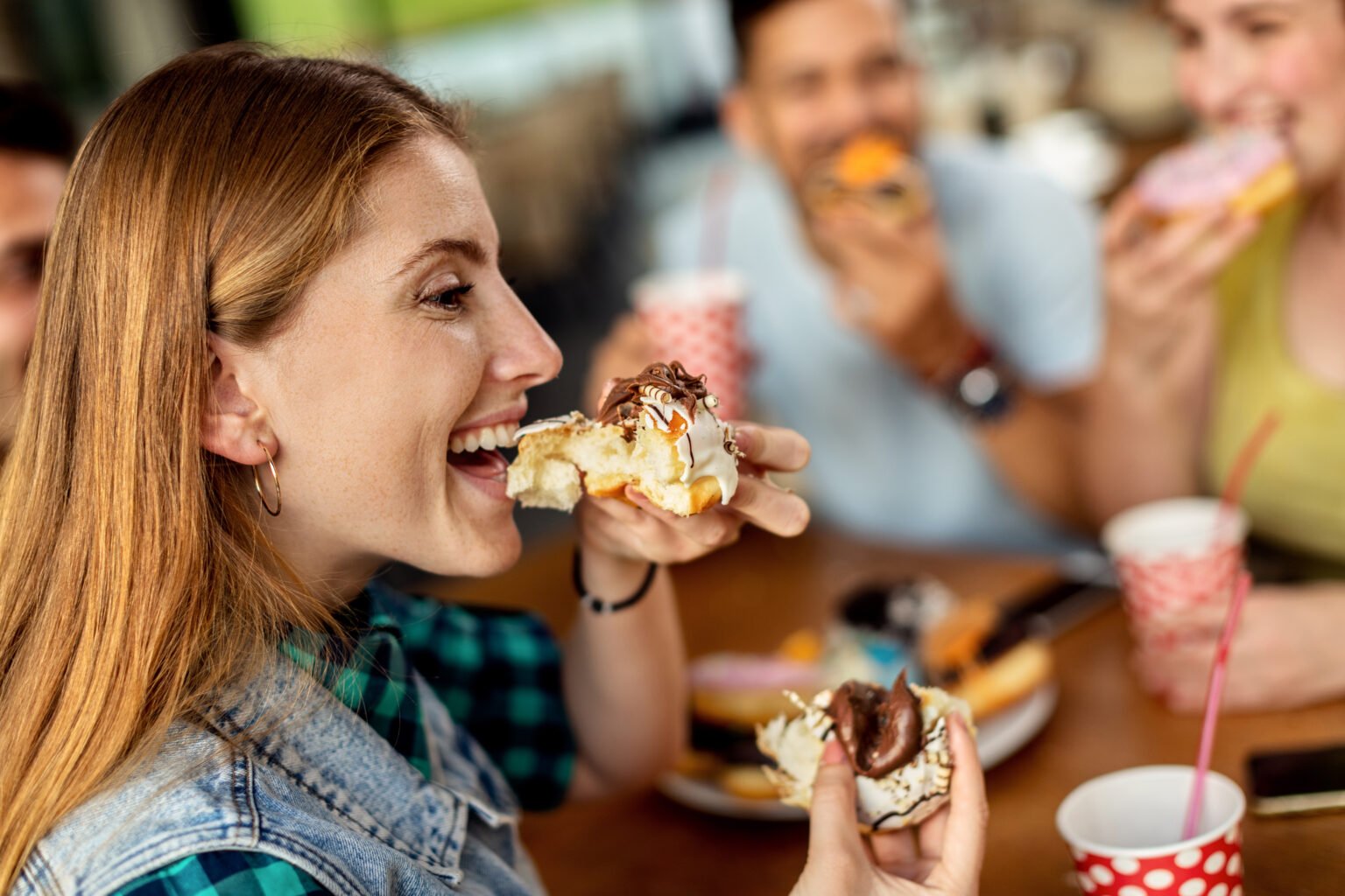 Happy woman and her friends eating glazed donuts in a cafe.